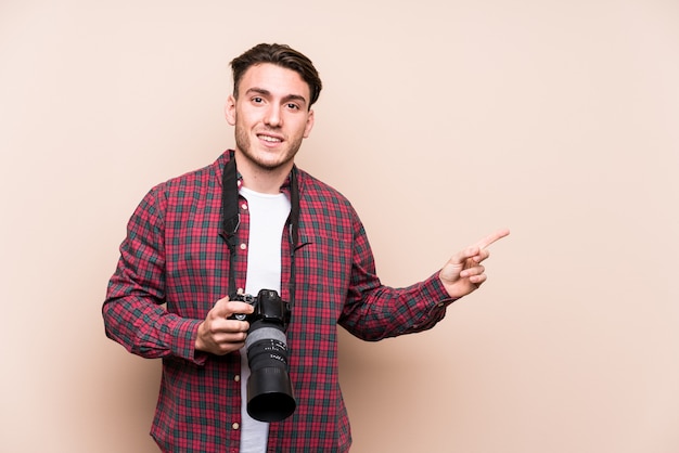 Hombre joven fotógrafo caucásico sonriendo y señalando a un lado, mostrando algo en el espacio en blanco.