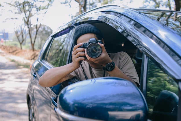Hombre joven fotógrafo tomando fotos mientras está sentado en un automóvil Hombre capturando una vista perfecta