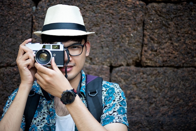 Hombre joven fotógrafo viajero con mochila tomando foto con su cámara