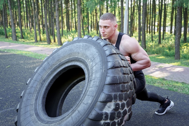 Hombre joven fuerte voltear el neumático mientras hace ejercicio al aire libre. CrossFit.