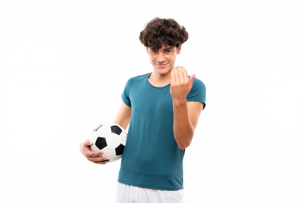 Hombre joven del futbolista sobre la pared blanca aislada que invita a venir con la mano. Feliz de que hayas venido