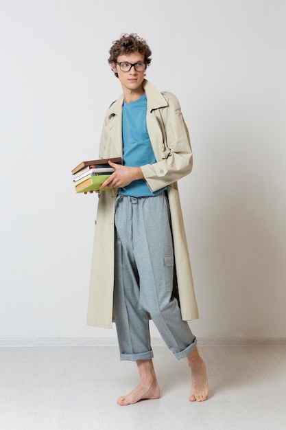 Foto hombre joven con gabardina con gafas y sosteniendo libros