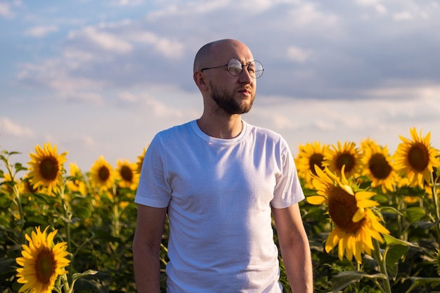 Hombre joven con gafas en un campo de girasoles al atardecer.