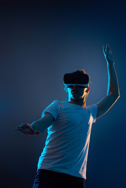 Hombre joven con gafas de realidad virtual jugando videojuegos sobre fondo azul oscuro. Luz de neón.