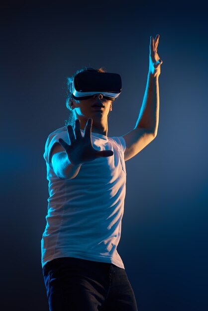 Hombre joven con gafas de realidad virtual sobre fondo azul oscuro. Luz de neón.