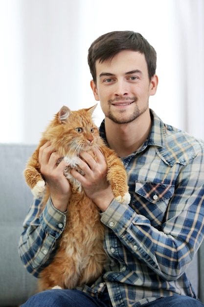 Hombre joven con gato mullido sentado en un sofá