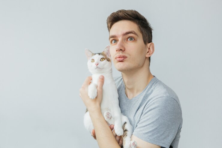 Hombre joven con gato sobre fondo gris claro. Mascota favorita. Hombre, tenencia, gato