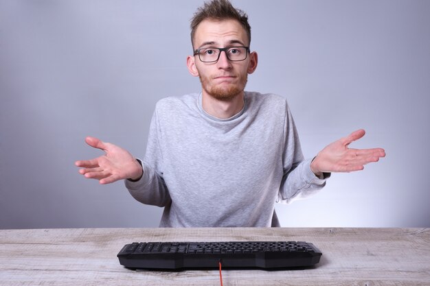 Foto hombre joven geek divertido que trabaja en la computadora. escribiendo en el programador del teclado en vidrios delante de la computadora.