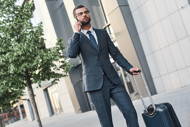 Hombre joven con glases y maleta llamando a un taxi