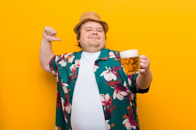 Hombre joven de gran tamaño con una pinta de cerveza contra la pared plana