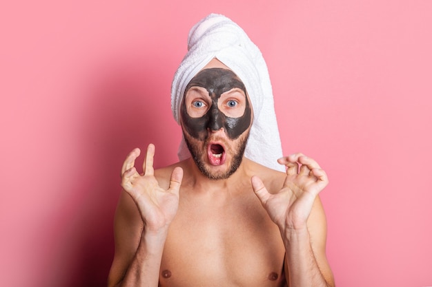Hombre joven gritando con máscara cosmética en su rostro sobre un fondo rosa