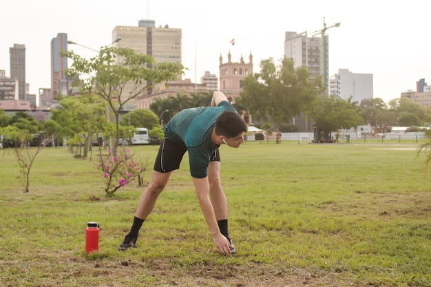 Hombre joven guapo con auriculares que se extiende en el parque con la ciudad de fondo.