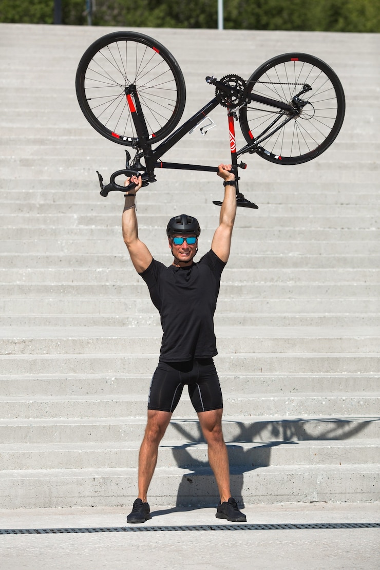 Hombre joven guapo con casco y gafas de sol sosteniendo una bicicleta