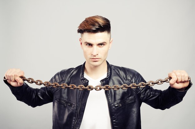 Foto hombre joven guapo en chaqueta de cuero con cadena de metal