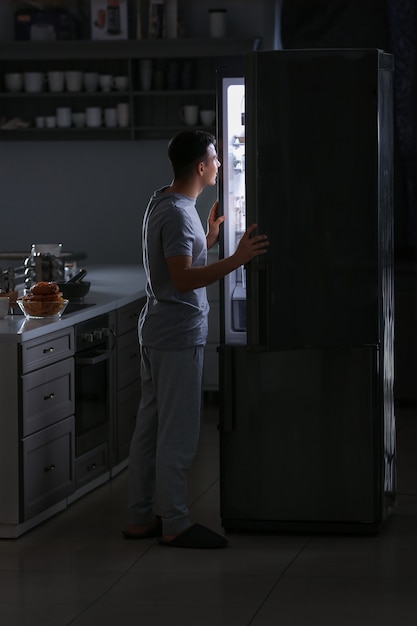 Foto hombre joven guapo eligiendo comida en el refrigerador por la noche