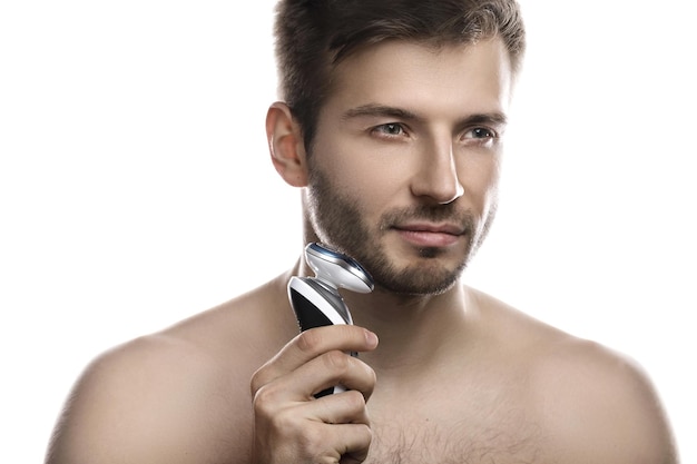 Hombre joven y guapo está utilizando una afeitadora eléctrica moderna sobre fondo blanco.