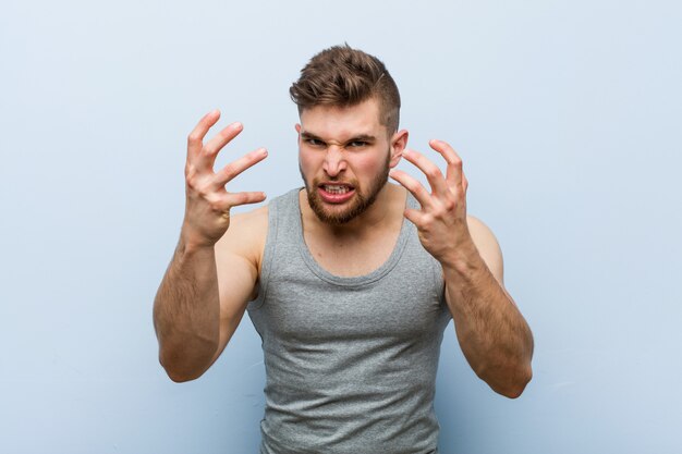 Foto hombre joven guapo fitness molesto gritando con las manos tensas.