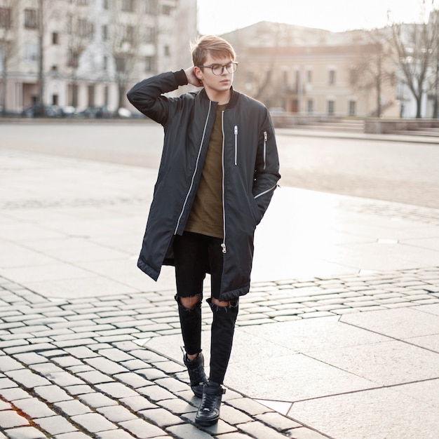 Hombre joven guapo con gafas en una chaqueta negra en jeans rotos