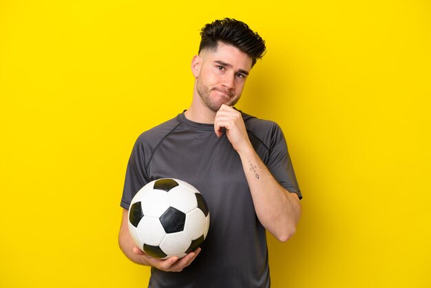 Hombre joven guapo jugador de fútbol aislado sobre fondo amarillo que tiene dudas y pensamiento