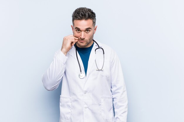 Hombre joven guapo médico con los dedos en los labios manteniendo un secreto.