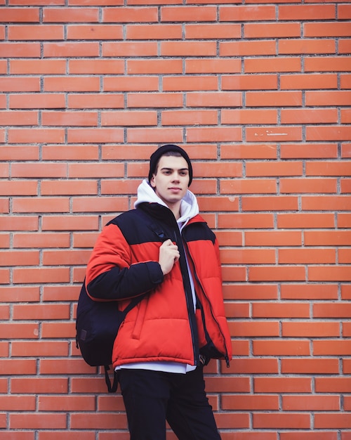 Hombre joven guapo con mochila en la pared de ladrillo rojo