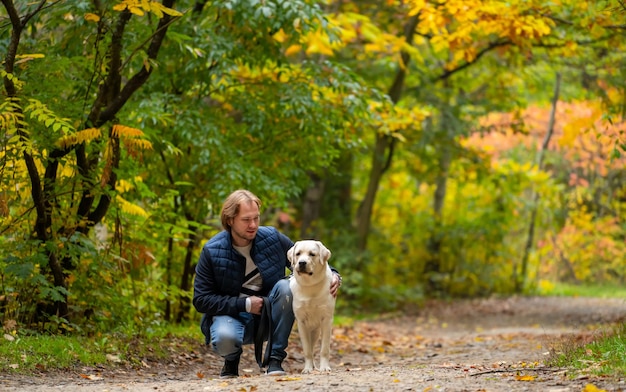 Hombre joven guapo con perro al aire libre. Hombre en un parque de otoño con perro labrador retriever.