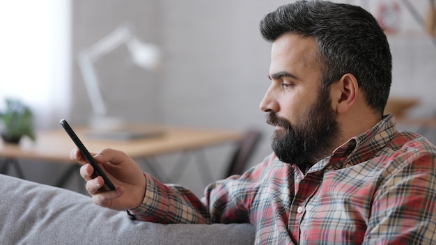 Hombre joven guapo con smartphone sentado en casa.