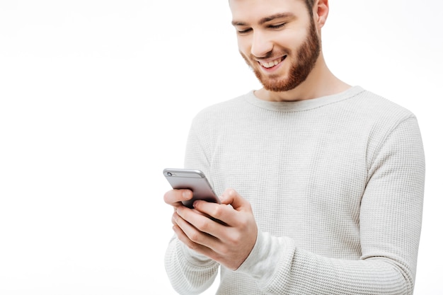 Hombre joven guapo con un suéter blanco usando el teléfono