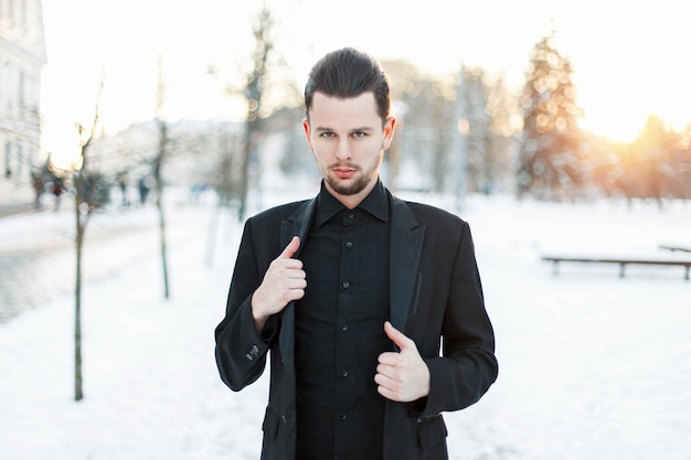 Hombre joven guapo con un traje negro al atardecer