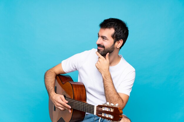 Foto hombre joven con guitarra sobre azul aislado mirando hacia el lado