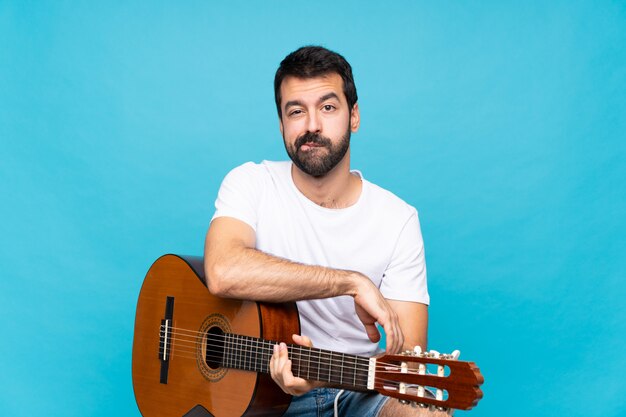 Hombre joven con guitarra sobre azul aislado sentirse molesto