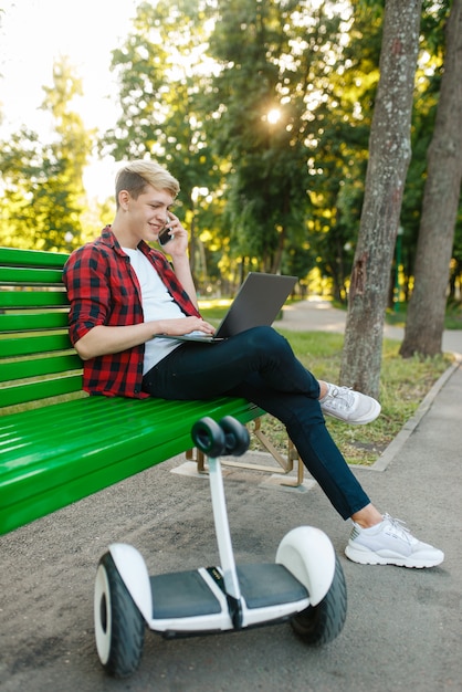 Hombre joven con gyroboard sentado en el banco en el parque.