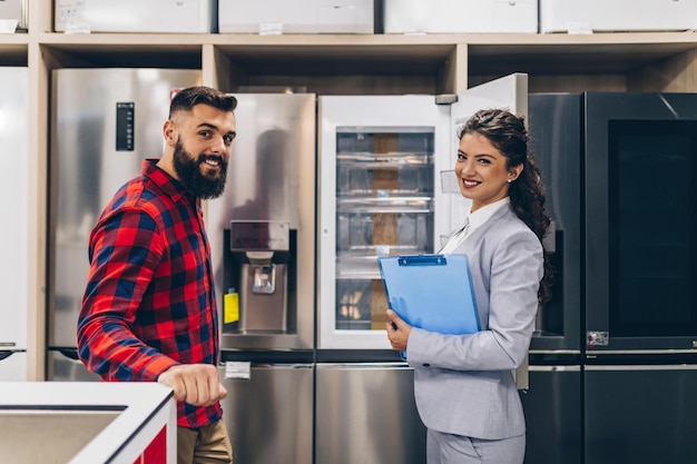 Hombre joven hablando con vendedora sobre refrigerador que quiere comprar.