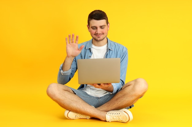 Hombre joven hablando por video comunicación en la computadora portátil sobre fondo amarillo.