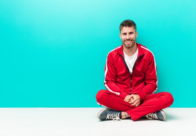 Hombre joven handosme con una sonrisa grande, amigable y despreocupada, con aspecto positivo, relajado y feliz, escalofriante contra la pared de color plano