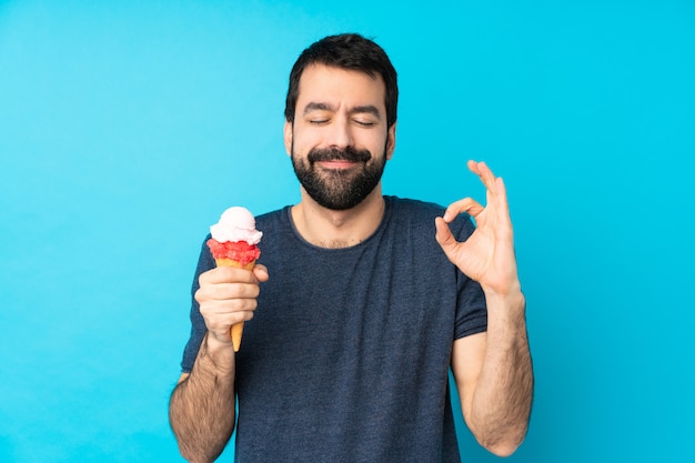 Hombre joven con un helado de cucurucho sobre azul en pose zen