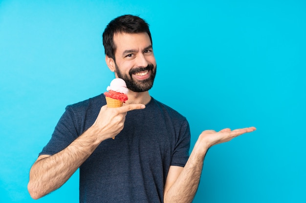 Hombre joven con un helado de cucurucho sobre azul sosteniendo copyspace imaginario en la palma