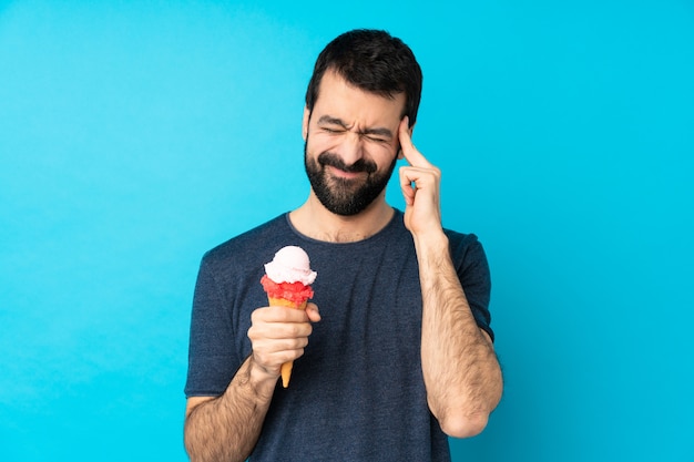 Hombre joven con un helado de cucurucho sobre pared azul aislada con dolor de cabeza