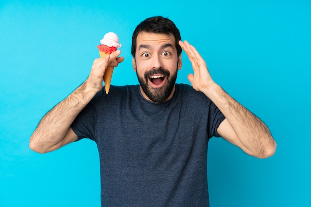 Hombre joven con un helado de cucurucho sobre pared azul aislado con expresión de sorpresa