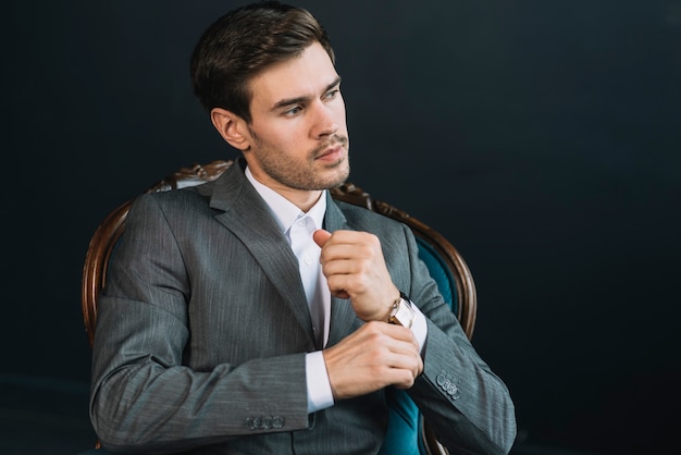 Un hombre joven hermoso atractivo que se sienta en silla del vintage contra fondo negro