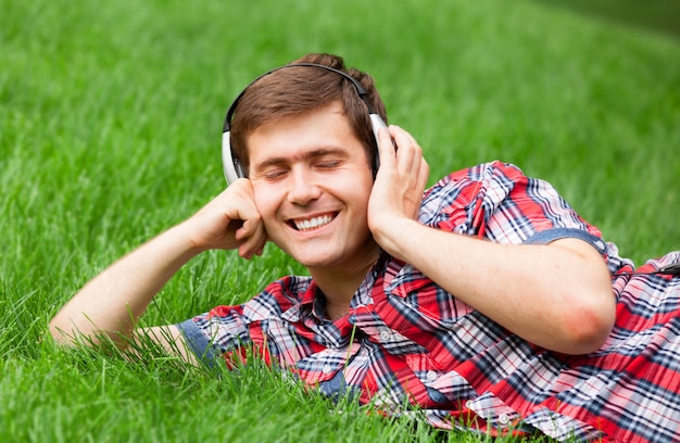 Hombre joven hermoso con los auriculares en la hierba verde