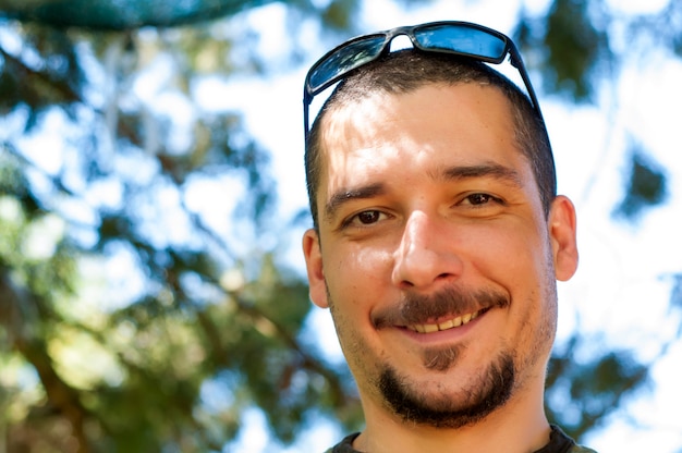 Hombre joven hermoso con el bigote y barba y gafas de sol que gozan en el parque