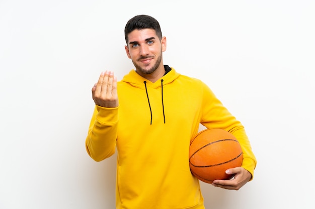 Hombre joven hermoso del jugador de básquet sobre la pared blanca aislada que invita a venir con la mano. feliz de que hayas venido