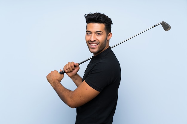 Hombre joven hermoso que juega a golf sobre la pared azul aislada