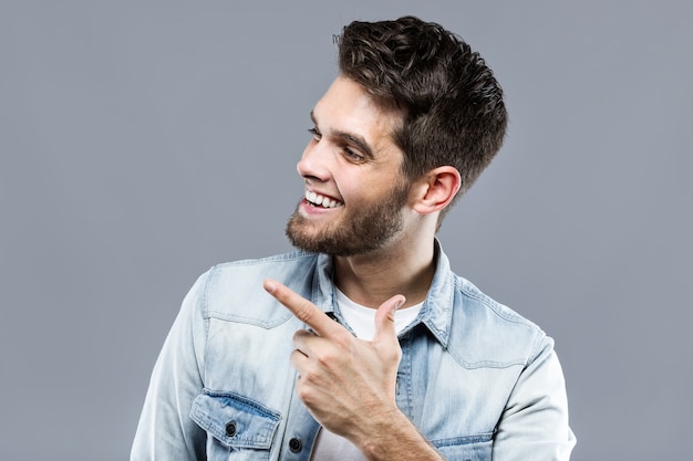 Hombre joven hermoso que presenta y que mira de lado sobre fondo gris.