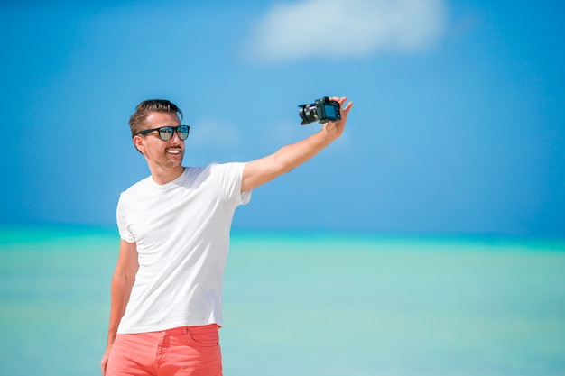 Hombre joven hermoso que toma una foto del uno mismo en la playa tropical