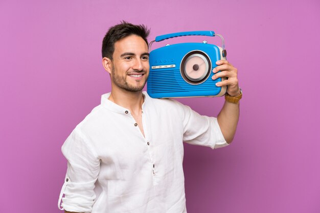 Hombre joven hermoso sobre púrpura que sostiene una radio