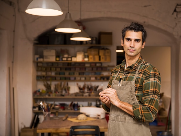 Hombre joven hermoso en el taller de la cerámica que sostiene la arcilla