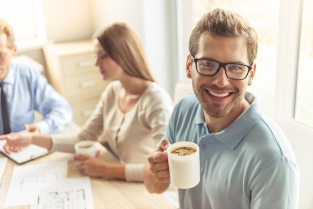 El hombre joven hermoso en vidrios está sosteniendo la taza de café.