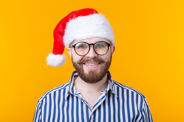 Hombre joven inconformista lindo loco alegre con sombrero rojo de santa claus posando sobre pared amarilla. El concepto de Navidad.